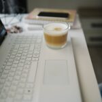 이른 아침 노트북 자판 위에 놓인 커피잔과 메모 노트, 스마트폰이 있는 책상